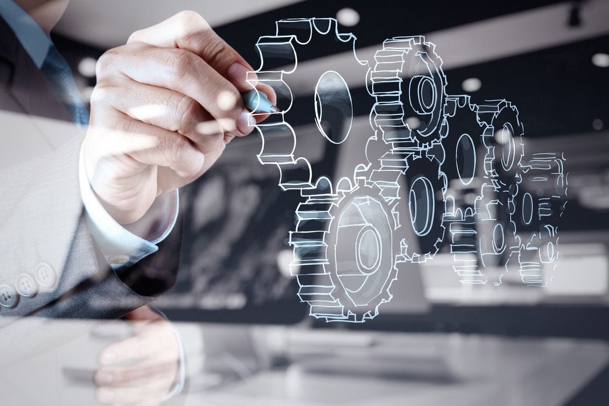 A businessman draws interlocking gears on a glass screen.