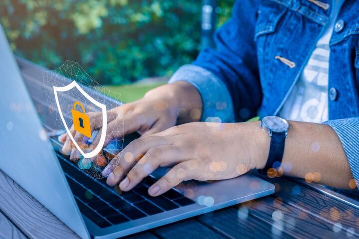 Hands on a laptop with a padlock and shield graphic.