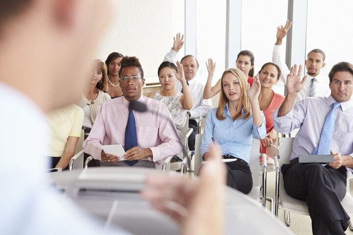 A conference audience raises hands to ask questions.