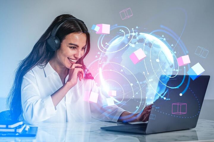 A woman at a laptop with a holographic globe above it.