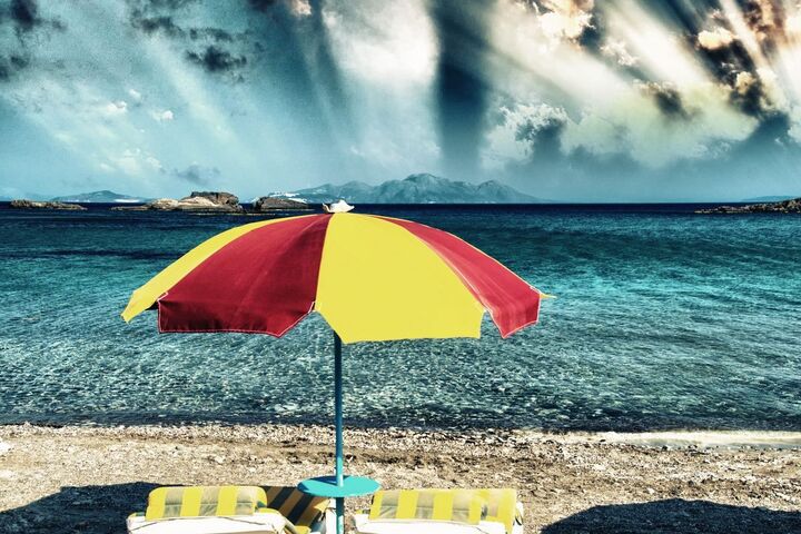 A striped beach umbrella on the sand under a stormy sky.