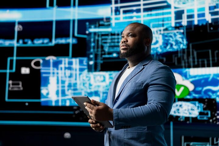 A man in a suit presenting beside a blue digital display.
